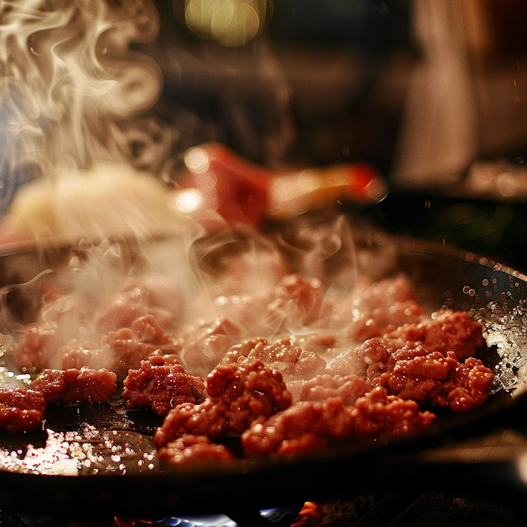 A close-up of ground beef being sizzled in a hot skillet, emitting steam and aroma
